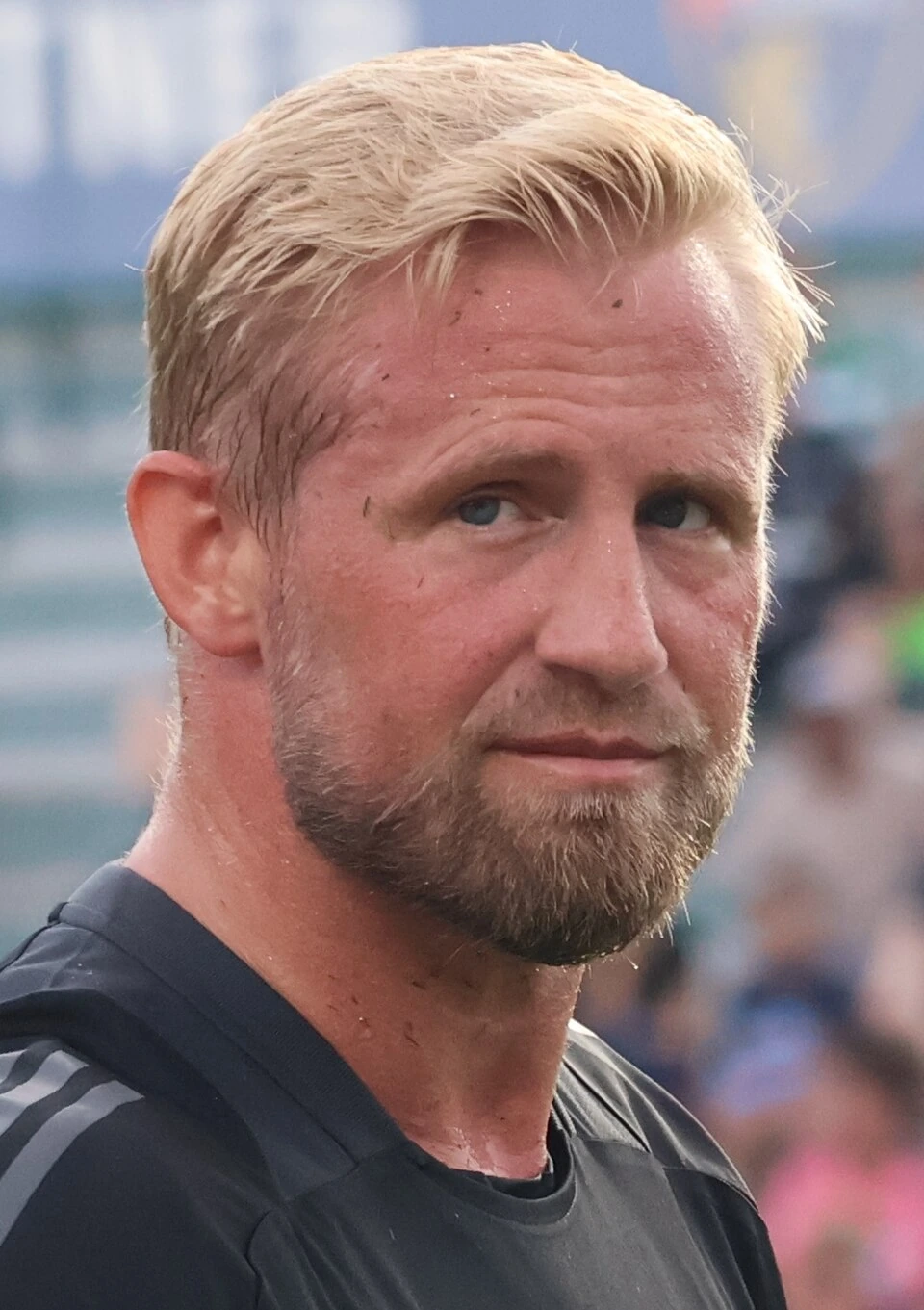 Close-up photo of Kasper Schmeichel in a black training top, outdoors with a blurred stadium background.