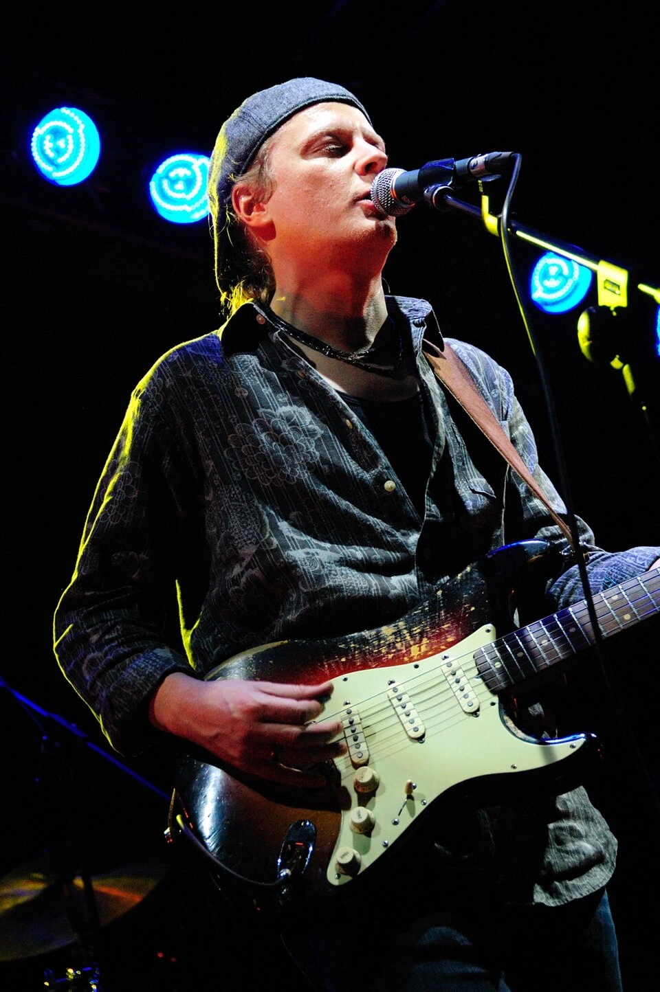 Matt Schofield performing on stage with an electric guitar and microphone