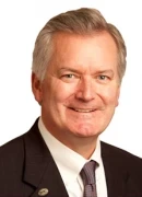 Headshot portrait of Daniel J. Schmechel smiling in a suit and tie against a white background.
